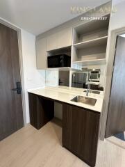 Compact modern kitchen with wooden and white cabinetry, built-in microwave, and stainless steel sink