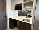 Compact modern kitchen with wooden and white cabinetry, built-in microwave, and stainless steel sink