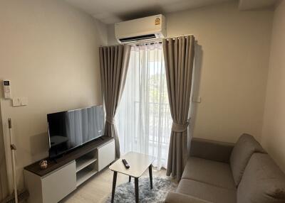 Modern living room with sofa, TV, and air conditioning, featuring a window with curtains