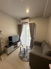 Modern living room with sofa, TV, and air conditioning, featuring a window with curtains