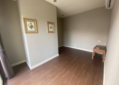 Empty room with brown wooden flooring, light grey walls, and two framed pictures