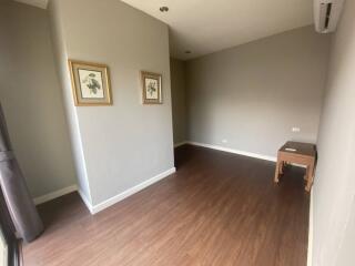 Empty room with brown wooden flooring, light grey walls, and two framed pictures