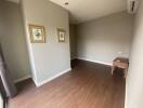 Empty room with brown wooden flooring, light grey walls, and two framed pictures