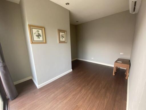 Empty room with brown wooden flooring, light grey walls, and two framed pictures