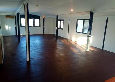 Spacious open-plan living area with dark wooden flooring, numerous windows, and column supports