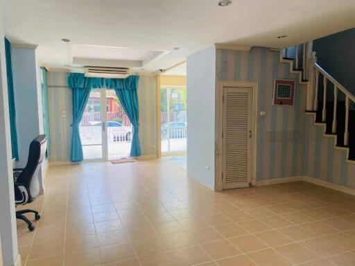 Spacious living room with tiled floor, blue curtains, and staircase