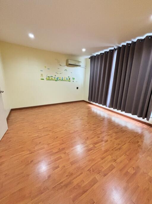 Spacious empty bedroom with wooden floor and dark curtains