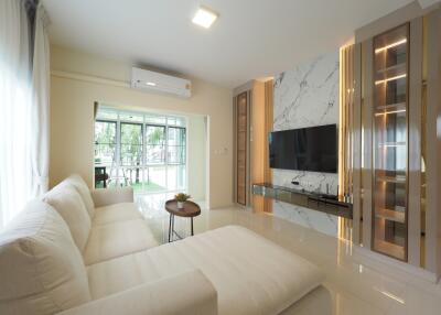 Modern living room with a white sectional sofa, wall-mounted TV, large windows, and contemporary lighting.