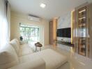 Modern living room with a white sectional sofa, wall-mounted TV, large windows, and contemporary lighting.