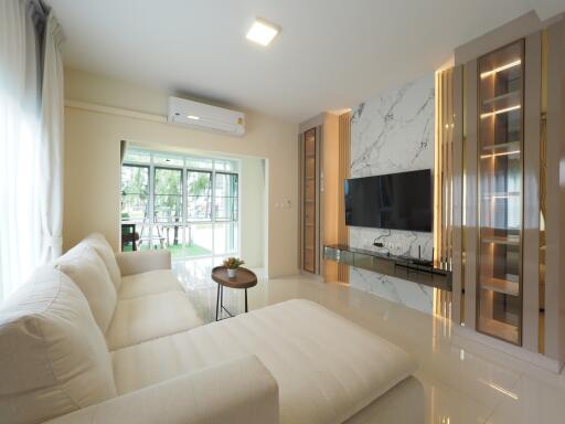 Modern living room with a white sectional sofa, wall-mounted TV, large windows, and contemporary lighting.