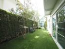 Side garden with lawn, trees, patio chairs, and a sunlit environment