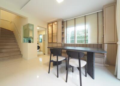 Modern dining area with wooden table and chairs next to a staircase and large windows