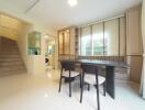 Modern dining area with wooden table and chairs next to a staircase and large windows