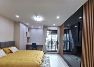 Spacious bedroom with a yellow bedspread, built-in desk, and large window leading to a balcony