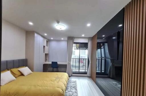 Spacious bedroom with a yellow bedspread, built-in desk, and large window leading to a balcony