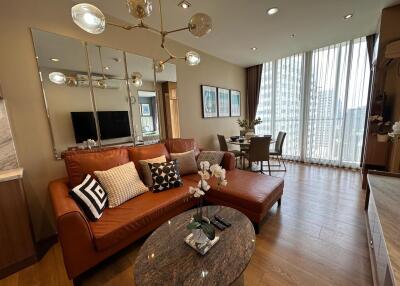 Modern living room with a brown leather sofa, a glass coffee table, and a dining area by the window.