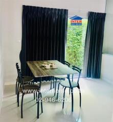 Dining area with a table and four chairs next to large windows with black curtains