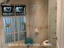 Bathroom with tiled walls and floor, featuring a glass shower door, window with decorative grills, toilet, and small fan.