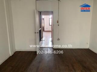 Empty bedroom with wooden floor and open door leading to another room