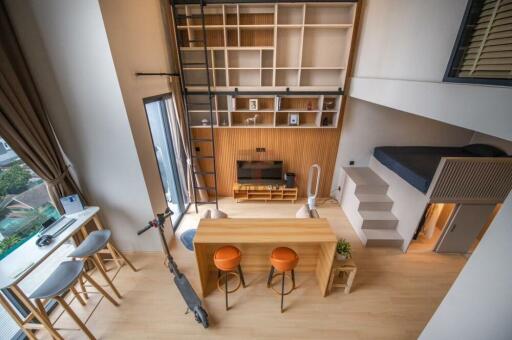 Modern loft-style living area with mezzanine bed, wood finishes, and natural lighting