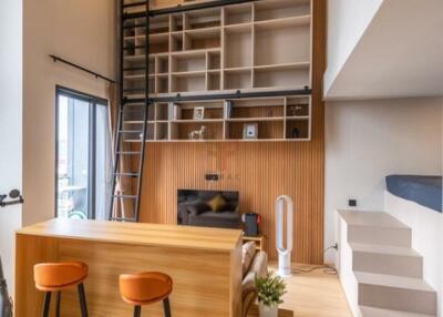 Modern living area with tall bookshelves, ladder, bar stools, and staircase