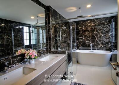 Modern bathroom with marble walls, freestanding bathtub, double sink vanity, and glass-enclosed shower