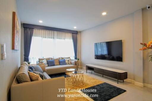 Modern living room with large windows, sofa, coffee table, and wall-mounted TV