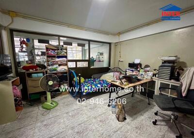 Bedroom with various furniture and items, including a bed, desk, chair, shelves, and fan