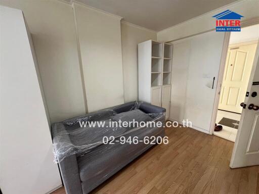 Small living room with a grey couch, white cabinets, and wooden flooring