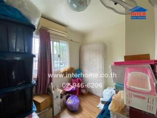 Small cluttered bedroom with storage boxes and a mattress against the wall