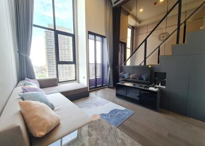 Modern living room with large windows, a comfortable couch, TV, and a loft area.