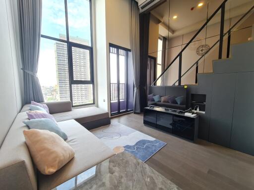 Modern living room with large windows, a comfortable couch, TV, and a loft area.