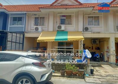 Front view of a residential building with a yellow and green awning and parked cars