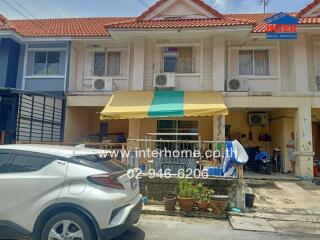 Front view of a residential building with a yellow and green awning and parked cars