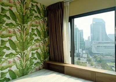 Bedroom with a green leaf-patterned wallpaper and a large window with city view