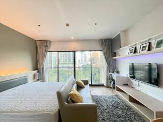 Modern bedroom with a large bed, sofa, TV, and city view