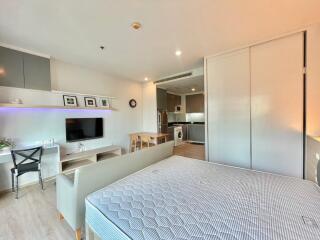 Modern studio apartment with bed, TV, dining area, and kitchenette