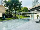 Outdoor swimming pool area with greenery and buildings in the background