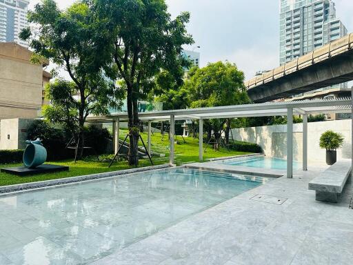 Outdoor swimming pool area with greenery and buildings in the background