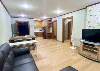 Modern living room with black leather furniture, wooden floor, and adjacent kitchen