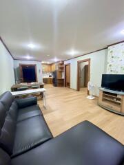 Modern living room with black leather furniture, wooden floor, and adjacent kitchen