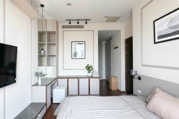 Modern bedroom with a neatly arranged bed and storage cabinet, wall-mounted TV, and minimalistic decor.