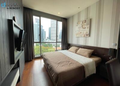 Modern bedroom with a large bed, wall-mounted TV, large window, and city view