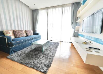 Living room with a sleek contemporary design featuring a blue sofa, glass coffee table, and wall-mounted TV.