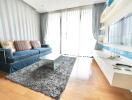 Living room with a sleek contemporary design featuring a blue sofa, glass coffee table, and wall-mounted TV.