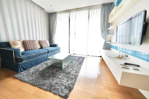 Living room with a sleek contemporary design featuring a blue sofa, glass coffee table, and wall-mounted TV.