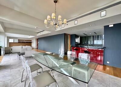 Modern open-plan dining and living space with glass-top table and chandelier