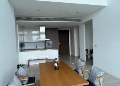 Modern dining area with wooden table and chairs, open kitchen in the background