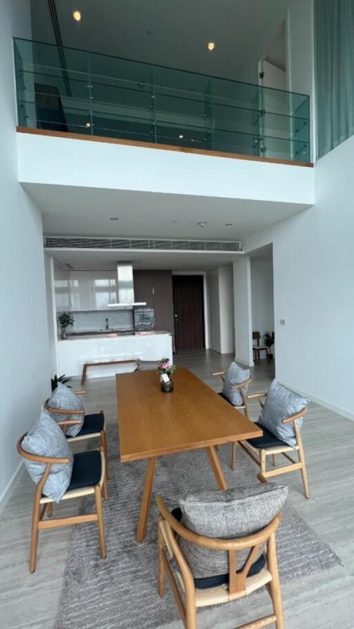 Modern dining area with wooden table and chairs, open kitchen in the background