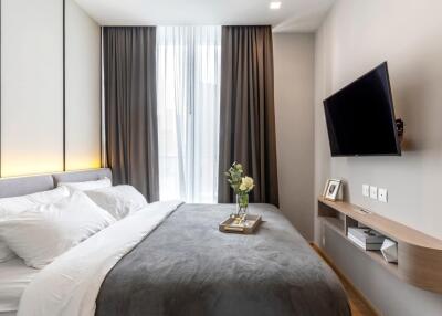 Modern bedroom with a large bed, wall-mounted TV, and a window with dark curtains